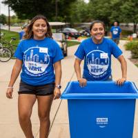 Two alumni with bin to move boxes in